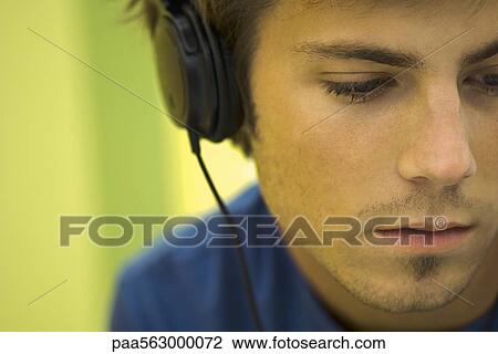 Young man listening to headphones, looking away View Large Photo Image Stock Image - Young man listening to headphones, looking away. Fotosearch
