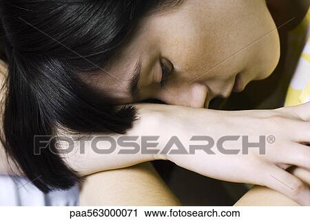 Stock Image - Young woman resting head on arms, close-up. Fotosearch