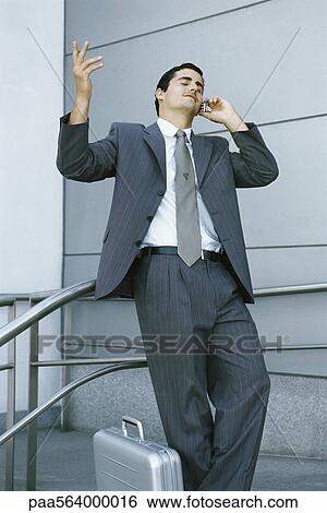 Stock Photograph - Businessman leaning against railing and using cell phone, making frustrated gesture with hand. Fotosearch