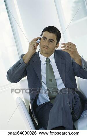 Businessman sitting with legs crossed, using cell phone View Large Photo Image Stock Photograph - Businessman sitting with legs crossed, using cell phone. Fotosearch