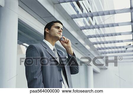 Stock Image - Businessman standing outside office building using cell phone. Fotosearch