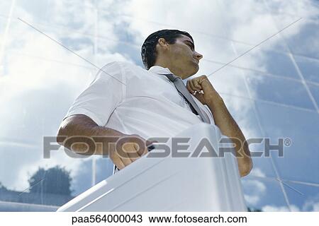 Businessman standing outside office building, carrying briefcase and adjusting collar, low angle view View Large Photo Image Stock Image - Businessman standing outside office building, carrying briefcase and adjusting collar, low angle view. Fotosearch