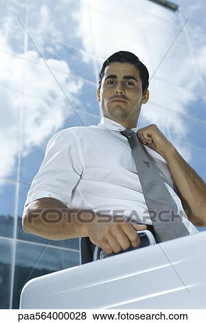 Businessman standing outside office building carrying briefcase, adjusting tie View Large Photo Image Stock Photo - Businessman standing outside office building carrying briefcase, adjusting tie. Fotosearch
