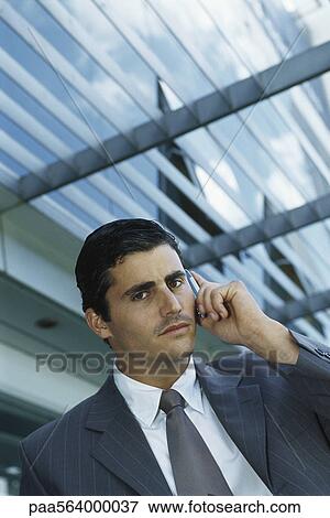 Stock Photo - Businessman standing outside office building using cell phone. Fotosearch