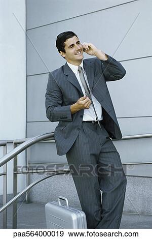 Stock Photo - Businessman using cell phone, leaning against railing. Fotosearch