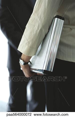 Stock Image - Businesswoman carrying briefcase under arm in conversation with colleague, mid section. Fotosearch