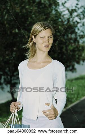 Stock Image - Woman carrying shopping bag, looking away and smiling. Fotosearch
