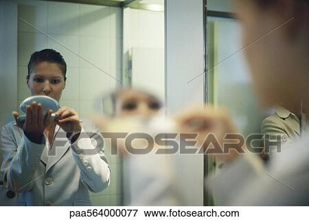 Stock Photo - Woman holding powder compact putting on makeup, over shoulder view. Fotosearch