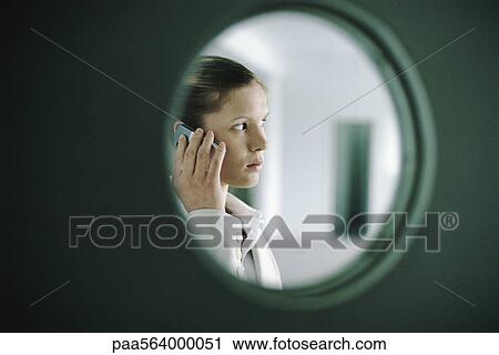 Stock Image - Woman using cell phone, viewed through window. Fotosearch