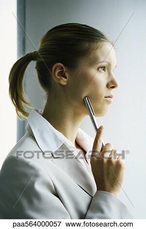 Stock Photo - Young businesswoman looking away in thought, holding pen up to face. Fotosearch