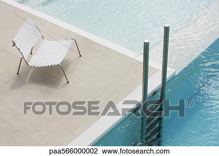 Stock Image - Chair at edge of pool near ladder. Fotosearch