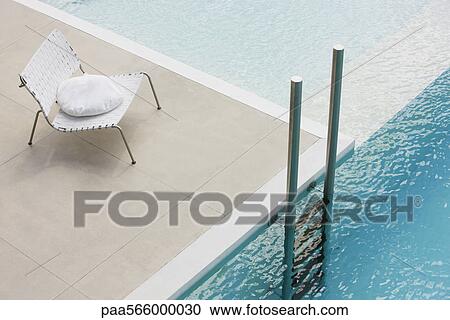 Stock Image - Chair with cushion at edge of pool near ladder. Fotosearch