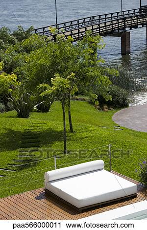 Stock Image - Sunbathing bed on poolside deck at resort. Fotosearch