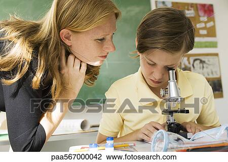 Boy looking through microscope, teacher watching View Large Photo Image Stock Image - Boy looking through microscope, teacher watching. Fotosearch