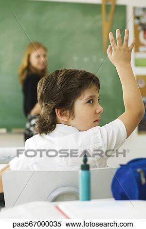 Stock Photography - Boy raising hand in class, looking over shoulder. Fotosearch