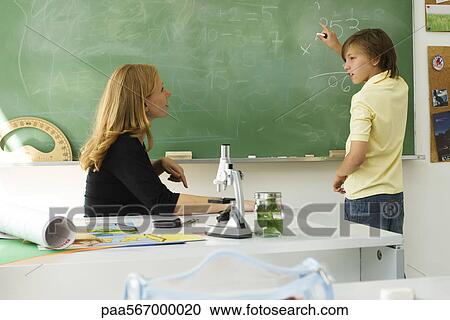 Boy solving math problem on blackboard, looking at teacher for assistance View Large Photo Image Stock Image - Boy solving math problem on blackboard, looking at teacher for assistance. Fotosearch