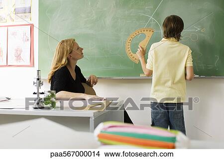 Boy standing in front of classroom blackboard, using protractor View Large Photo Image Picture - Boy standing in front of classroom blackboard, using protractor. Fotosearch