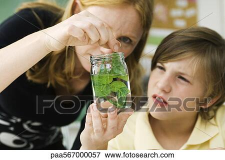 Stock Photo - Elementary teacher showing student plant specimen in jar. Fotosearch