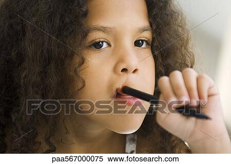 Stock Photography - Little girl holding pen against mouth, looking away. Fotosearch