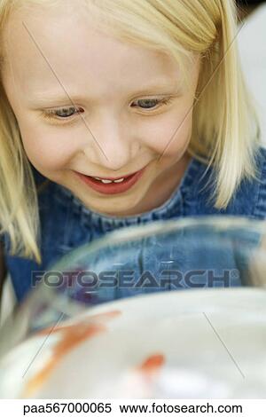 Stock Photography - Little girl looking at goldfish in bowl, high angle view. Fotosearch