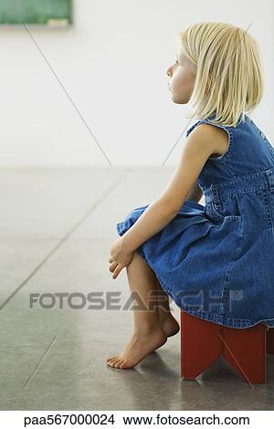 Picture - Little girl sitting on stool, looking away in thought. Fotosearch