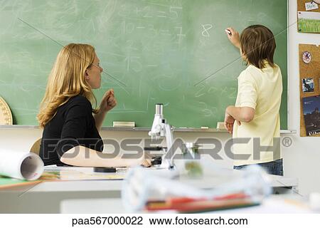 Teacher watching boy writing on blackboard View Large Photo Image Stock Image - Teacher watching boy writing on blackboard. Fotosearch