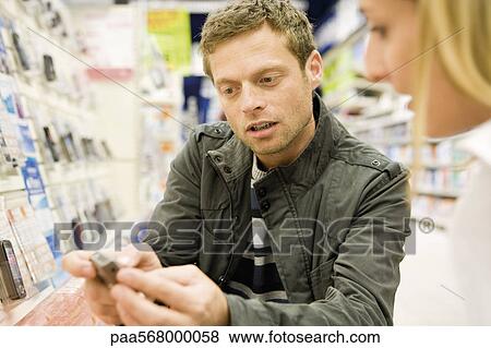 Couple shopping together, man showing cell phone to woman View Large Photo Image Stock Photo - Couple shopping together, man showing cell phone to woman. Fotosearch