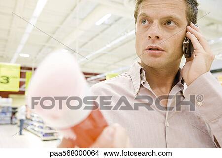 Man in supermarket using cell phone, choosing bottle of shower gel View Large Photo Image Picture - Man in supermarket using cell phone, choosing bottle of shower gel. Fotosearch