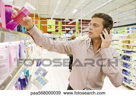 Man using cell phone, selecting bottle of shower gel from supermarket shelf View Large Photo Image Stock Photo - Man using cell phone, selecting bottle of shower gel from supermarket shelf. Fotosearch
