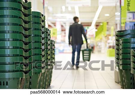 Picture - Shopping baskets stacked in rows, shopper in background. Fotosearch