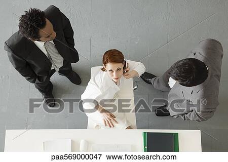 Businesswoman making phone call with colleagues standing nearby View Large Photo Image Stock Photo - Businesswoman making phone call with colleagues standing nearby. Fotosearch