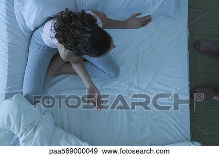 Stock Photo - Couple in conflict, woman sitting on bed with arms out in frustration. Fotosearch