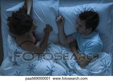 Stock Image - Couple lying together in bed, woman watching man sleeping. Fotosearch
