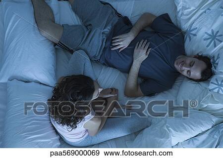 Couple relaxing together in bed View Large Photo Image Stock Photo - Couple relaxing together in bed. Fotosearch