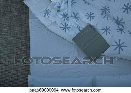 Picture - Open book lying face down on empty bed. Fotosearch