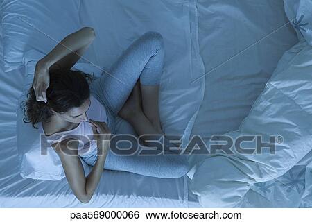 Stock Photograph - Woman sitting in bed taking temperature. Fotosearch