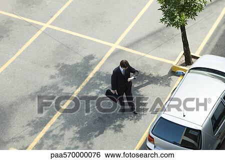 Businessman checking time as he walks to parked car View Large Photo Image Stock Photograph - Businessman checking time as he walks to parked car. Fotosearch