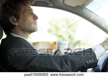 Stock Image - Businessman driving to work with cup of coffee in hand. Fotosearch