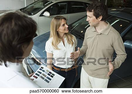 Couple in car dealership showroom discussing new car options with salesman View Large Photo Image Stock Image - Couple in car dealership showroom discussing new car options with salesman. Fotosearch