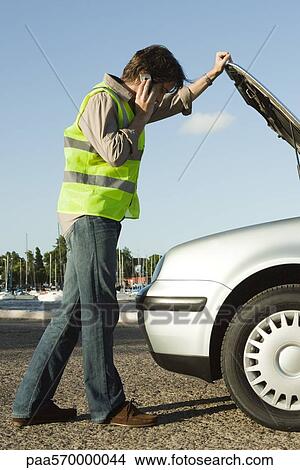 Man making phone call with cell phone while evaluating car broken down on side of road View Large Photo Image Picture - Man making phone call with cell phone while evaluating car broken down on side of road. Fotosearch