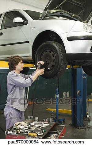 Picture - Mechanic changing tires of car elevated on hydraulic lift. Fotosearch