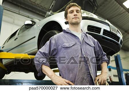 Mechanic in auto repair shop, car on hydraulic lift in background View Large Photo Image Stock Photo - Mechanic in auto repair shop, car on hydraulic lift in background. Fotosearch