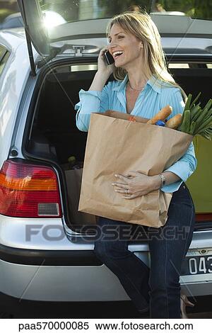 Woman sitting in open hatchback with bag of groceries on lap making phone call View Large Photo Image Stock Photography - Woman sitting in open hatchback with bag of groceries on lap making phone call. Fotosearch