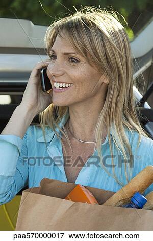 Woman using cell phone and carrying bag of groceries View Large Photo Image Stock Photo - Woman using cell phone and carrying bag of groceries. Fotosearch