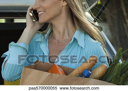 Woman using cell phone and holding bag of groceries View Large Photo Image Stock Photography - Woman using cell phone and holding bag of groceries. Fotosearch
