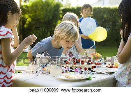 Boy blowing candles on birthday cake at outdoor birthday party View Large Photo Image Stock Photo - Boy blowing candles on birthday cake at outdoor birthday party. Fotosearch