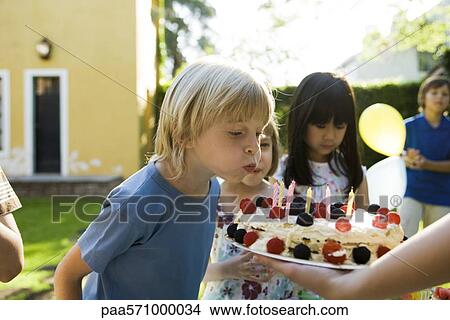 Boy blowing out candles on birthday cake at outdoor birthday party View Large Photo Image Picture - Boy blowing out candles on birthday cake at outdoor birthday party. Fotosearch