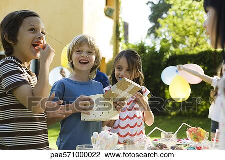 Stock Image - Boy opening gift and smiling with pleasure at birthday party. Fotosearch