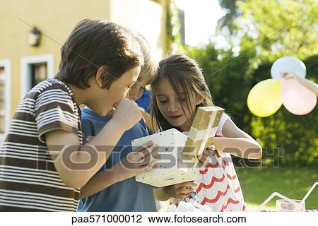 Boy opening gift at birthday party as friends watch View Large Photo Image Stock Image - Boy opening gift at birthday party as friends watch. Fotosearch