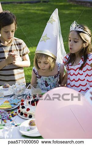 Girl blowing out candles on birthday cake at outdoor birthday party View Large Photo Image Stock Image - Girl blowing out candles on birthday cake at outdoor birthday party. Fotosearch